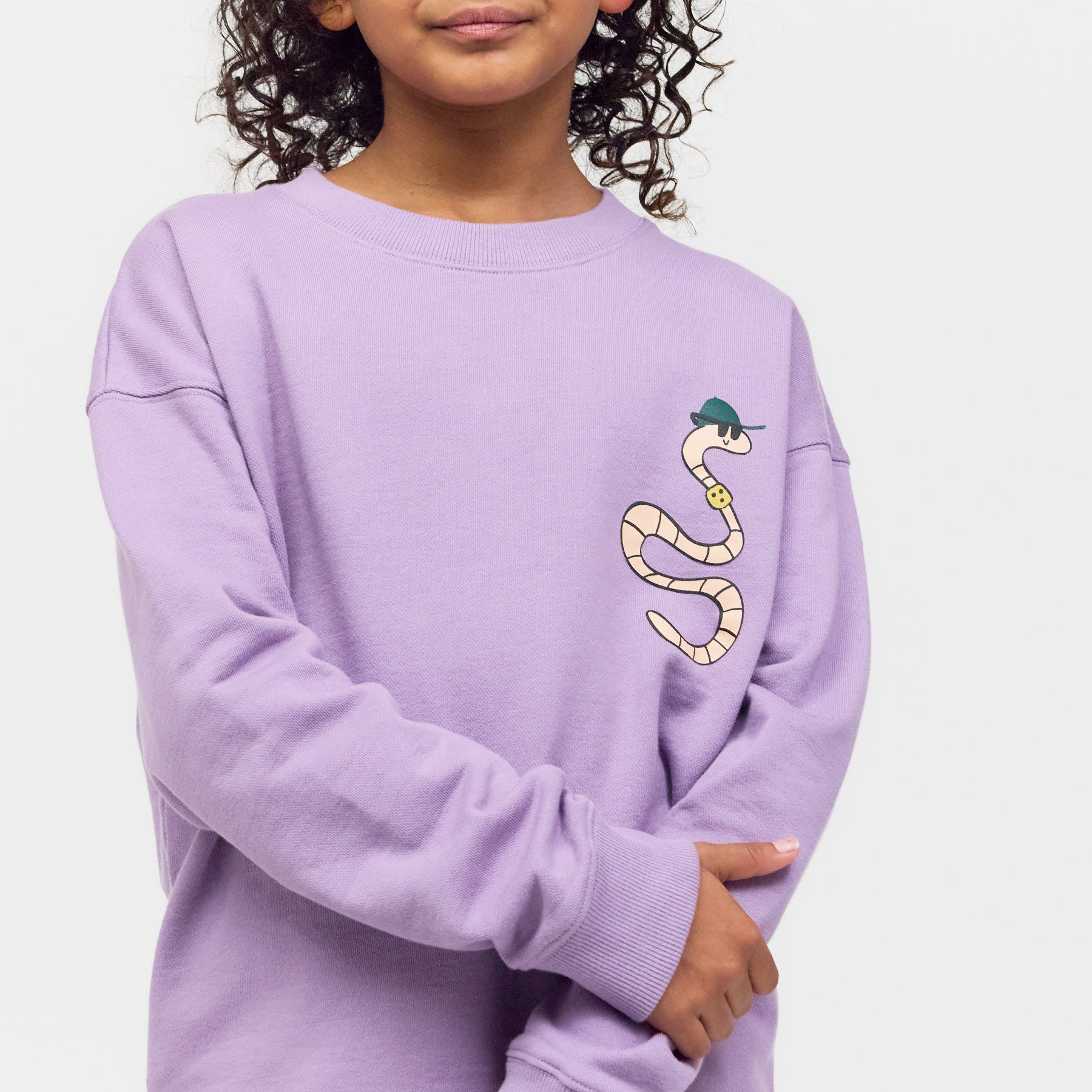 Kind trägt das lila Checker Tobi Sweatshirt mit Regenwurm-Grafik – gemütlicher Style zum 3. Kinofilm Die heimliche Herrscherin der Erde aus nachhaltiger 100% Bio-Baumwolle.